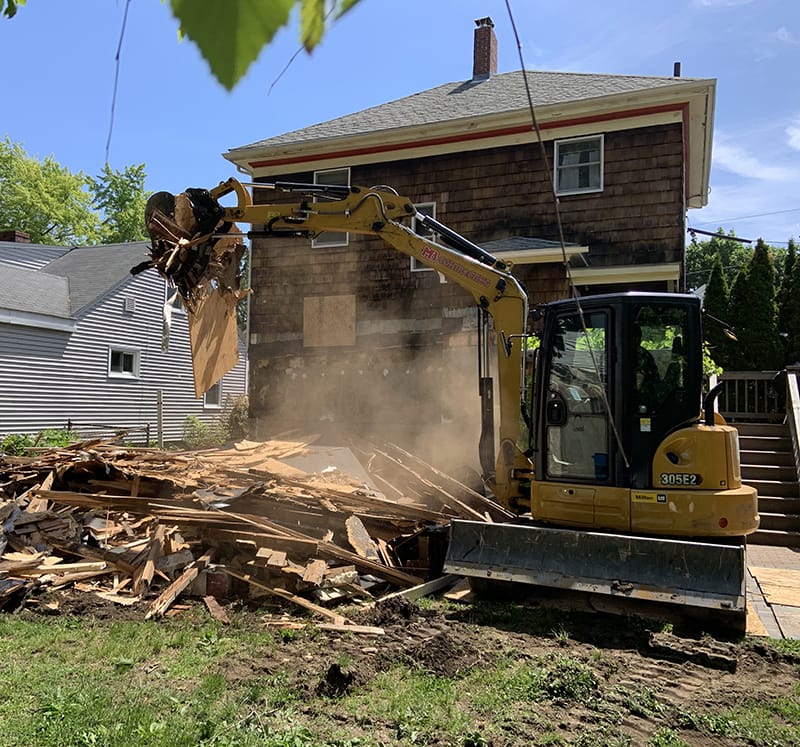 An excavator performing demolition services on a wooden structure.